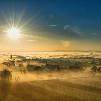 Vogelperspektive auf einen Sonnenaufgang über einer Winterlandschaft in sanftem Nebel