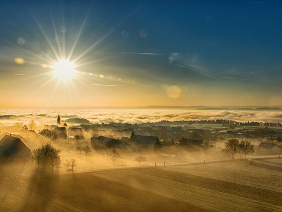 Vogelperspektive auf einen Sonnenaufgang über einer Winterlandschaft in sanftem Nebel