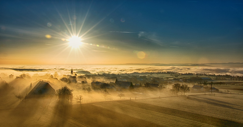 Vogelperspektive auf einen Sonnenaufgang über einer Winterlandschaft in sanftem Nebel